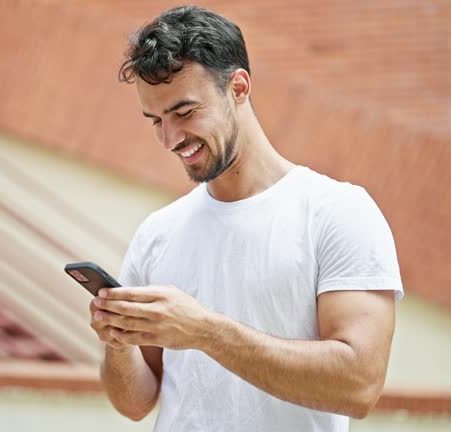 young hispanic man using smartphone with winner gesture at street